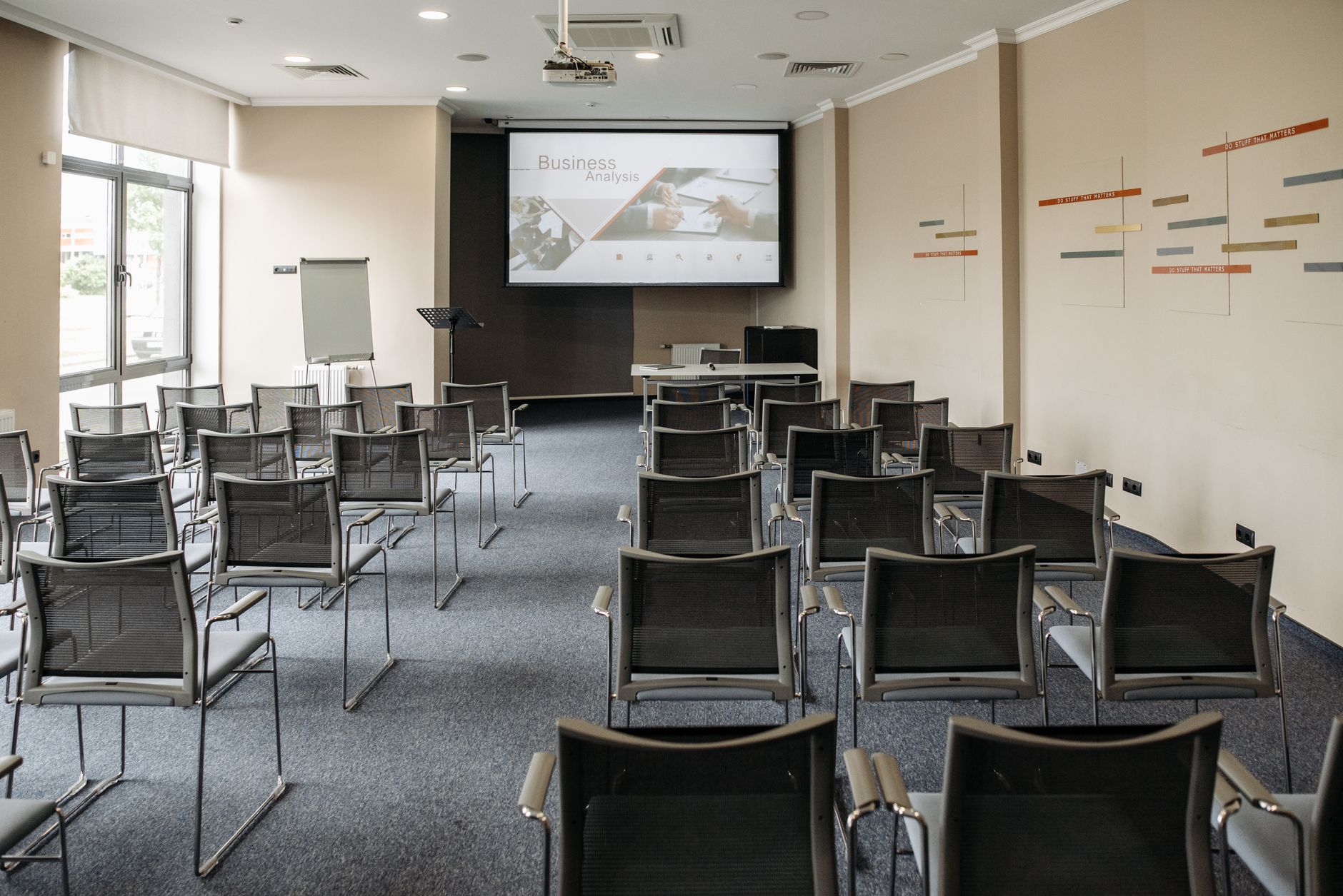 A minimalist professional conference room with large clear windows and a board monitor showing metrics